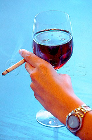 Hand holding glass of red wine and   cigarette