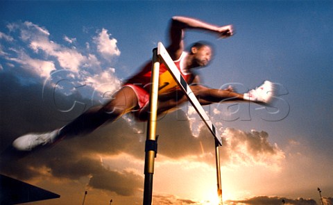 Runner clearing hurdle against blue sky at sunset