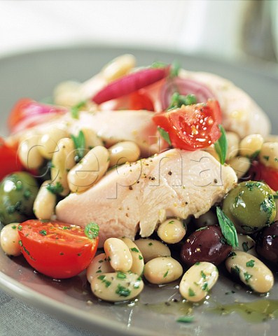 A plate of poached chicken with cannelini beans and olives