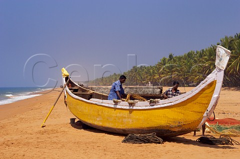 Fishermen busy with their nets and boat on palm fringed beach north of Thiruvananthapuram Trivandrum Kerala India