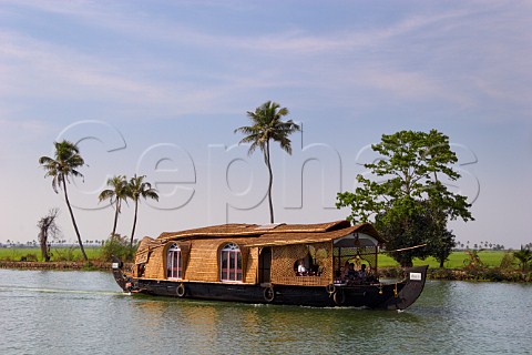 Houseboat cruising the Kuttanad the backwaters of Kerala known as the Venice of the East with lush green paddy fields beyond Kerala India