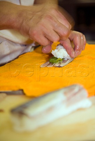 Adding rice to a layer of oba leaves while making mackerel sushi in a Japanese restaurant