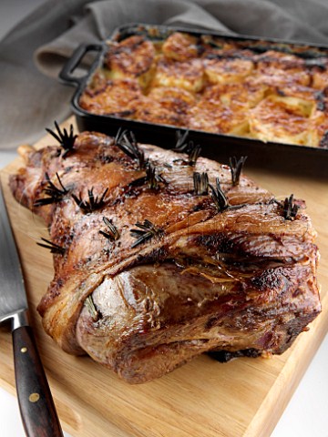 Roast leg of lamb on a chopping board with dauphinoise potatoes