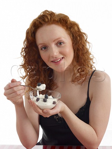 Young woman with bowl of yoghurt and blueberries for breakfast