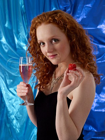 Young woman holding a glass of ros champagne and a strawberry