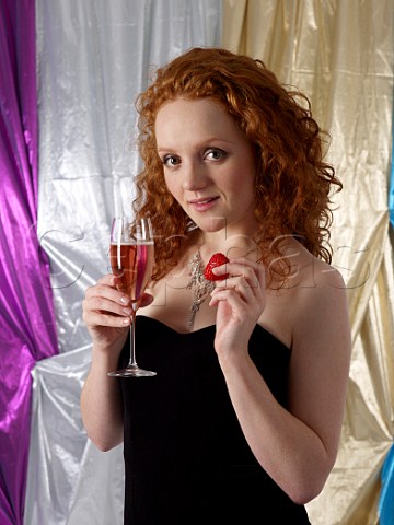 Young woman holding a glass of ros champagne and a strawberry