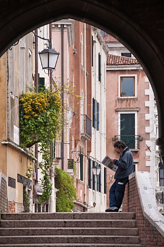 Man reading morning newspaper on canal bridge San Polo Venice Italy