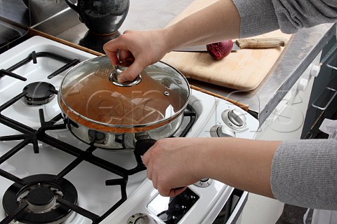 Putting a lid on a saucepan of simmering chicken rogan josh