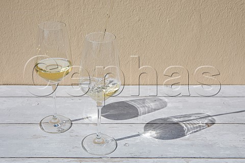 Two glasses of Riesling standing on a wooden table with wine being poured into one of the glasses
