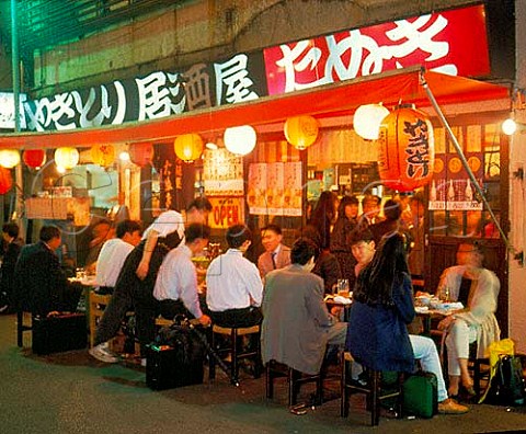 People eating and drinking outside a YakiTori   restaurant selling mainly grilled chicken in the   Ginza district of Tokyo  The red lanterns are   typical of this type of cheap eating place
