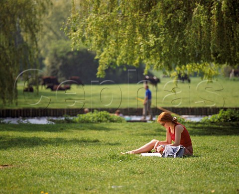 Girl studying on Laundress Green with Mill Pool   canal behind  Cambridge