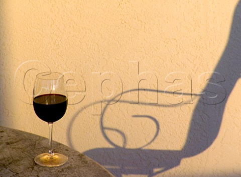 Red wine glass on terrace table with garden chair   shadow Florida USA