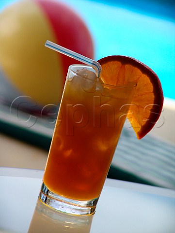 Glass of iced orange juice with pool  beach ball   behind  Florida USA