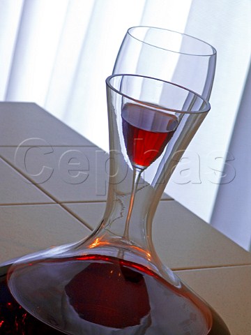 Glass of red wine viewed through the neck of a   decanter