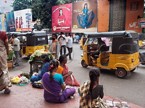Busy street life women making flower garlands men   selling fruit as traffic passes by Chennai   Madras India