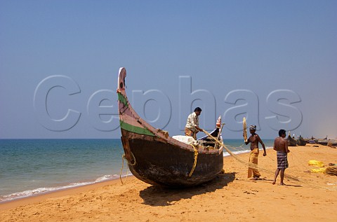 Fishermen busy with their nets and boat on the beach north of Thiruvananthapuram Trivandrum Kerala India