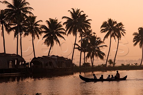 Men in a canoe passing moored houseboats sunrise on the Kuttanad the backwaters of Kerala known as the Venice of the East Kerala India