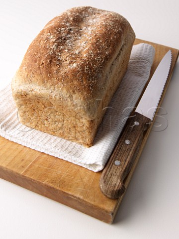 Brown loaf on breadboard with knife