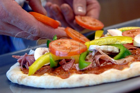 Adding sliced tomatoes peppers ham and salami to a pizza base