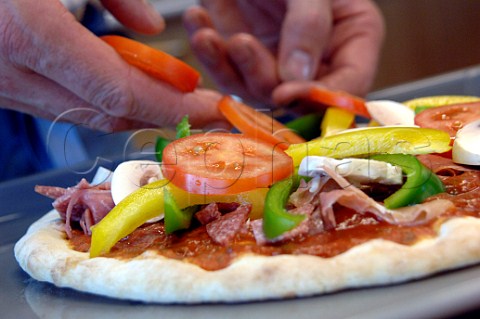 Adding sliced tomatoes peppers ham and salami to a pizza base
