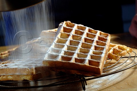 Making waffles dusting them with icing sugar when cooked
