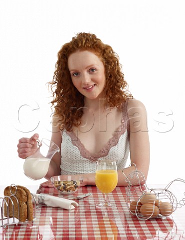 Young woman sitting at breakfast table fruit and nut muesli with milk wholemeal toast boiled eggs orange juice