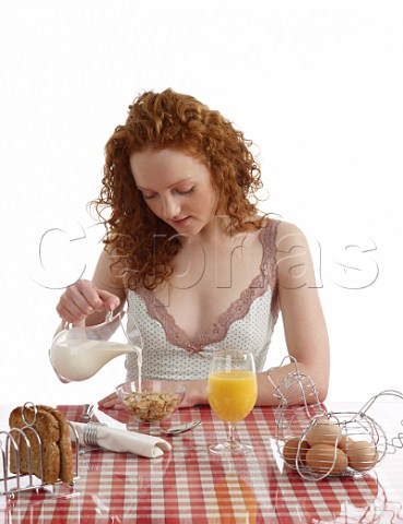 Young woman sitting at breakfast table Special K with milk wholemeal toast boiled eggs orange juice