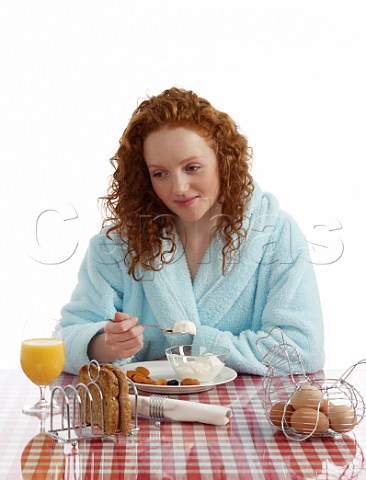 Young woman sitting at breakfast table yoghurt with dried fruits wholemeal toast boiled eggs orange juice