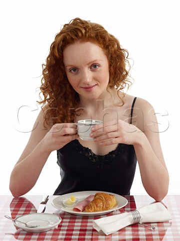 Young woman sitting at breakfast table croissant with ham and butter cup of black coffee