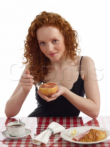 Young woman sitting at breakfast table pink grapefruit croissant with ham and butter cup of black coffee