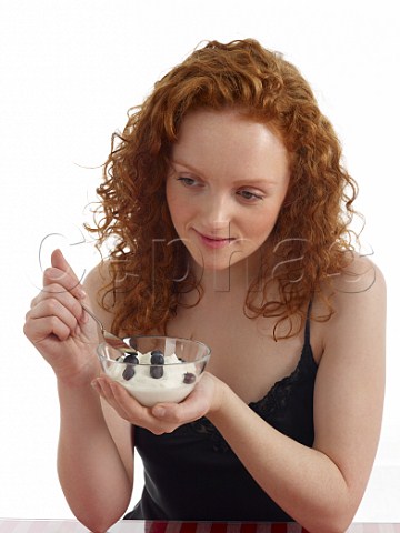 Young woman with bowl of yoghurt and blueberries for breakfast