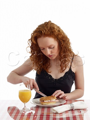 Young woman at breakfast table bagel with ham and cream cheese glass of orange juice