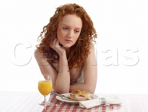 Young woman at breakfast table bagel with ham and cream cheese glass of orange juice