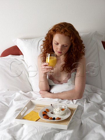 Young woman having breakfast in bed yoghurt and dried fruits glass of orange juice