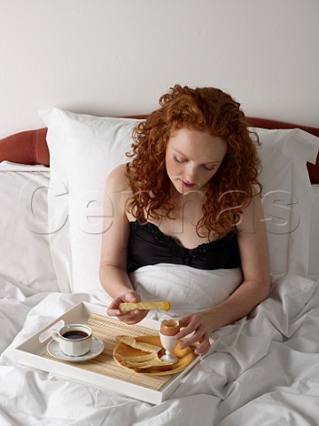 Young woman having breakfast in bed boiled egg with white bread soldiers cup of black coffee