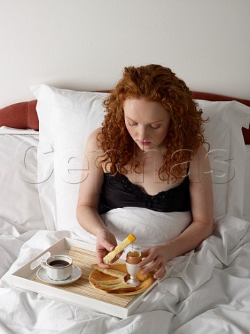 Young woman having breakfast in bed boiled egg with white bread soldiers cup of black coffee