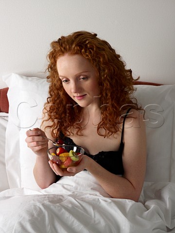 Young woman having breakfast in bed bowl of fresh fruit salad