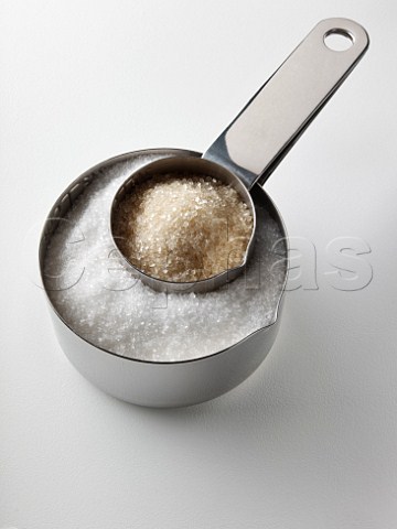 Granulated white sugar and unrefined cane sugar in steel measuring cups
