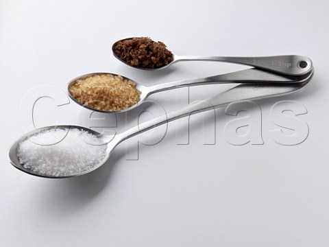 White granulated demerara and dark brown sugar in measuring spoons