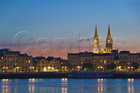 Lights of Quai des Chartrons reflecting in the Garonne river at dusk with the spires of StLouis church behind Bordeaux Gironde France