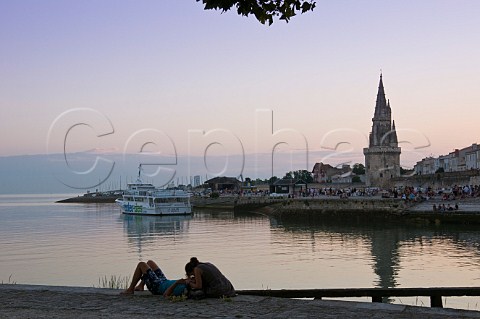 Couple sitting at the harbour entrance at dusk opposite the old prison tower La Rochelle CharenteMaritime France
