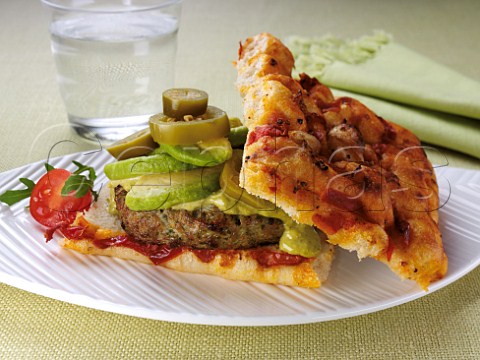 A mediterranean pork burger with avocado slices and foccacia bread