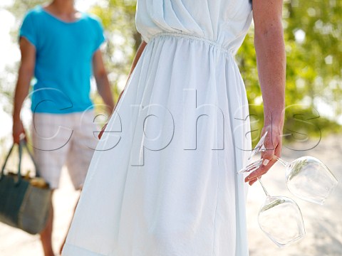 Young woman carrying wine glasses for a beach picnic