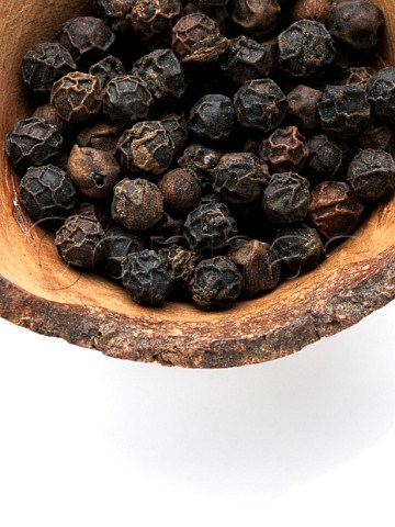 Close up of black peppercorns in a wooden bowl on a white bckground