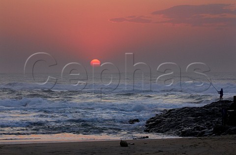 Sunrise over the Indian Ocean with man fishing from the rocks  Amanzimtoti KwaZuluNatal South Africa