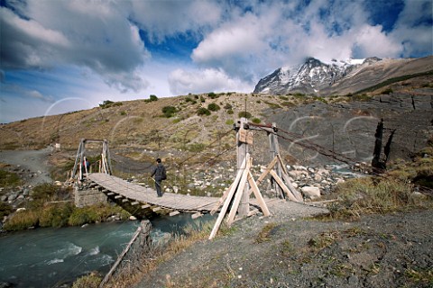 Trekkers crossing a small bridge on a trail in the Torres Del Paine National Park with Monte Almirante Nieto in the distance Patagonia Chile