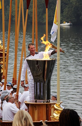 Friday 27 July 2012 Sir Matthew Pinsent lighting the cauldron on the Gloriana rowbarge on the River Thames at Hampton Court ready for it to be carried to London The rowers are holding their oars aloft  England
