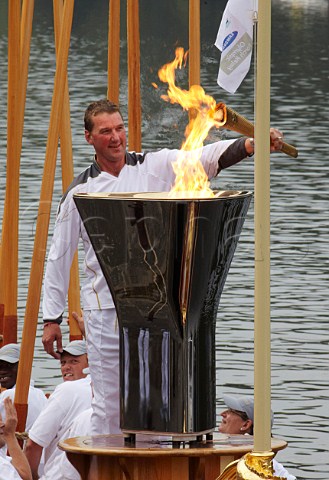 Friday 27 July 2012 Sir Matthew Pinsent lighting the cauldron on the Gloriana rowbarge on the River Thames at Hampton Court ready for it to be carried to London The rowers are holding their oars aloft  England