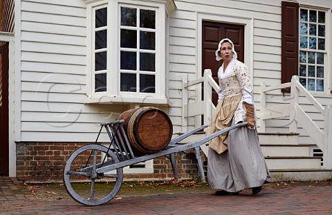 Woman in traditional dress wheeling a rum barrel Colonial Williamsburg Virginia USA
