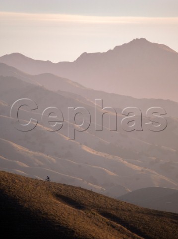 Mountain biker riding a ridge in the Wither Hills with the Blairich Range beyond Marlborough New Zealand